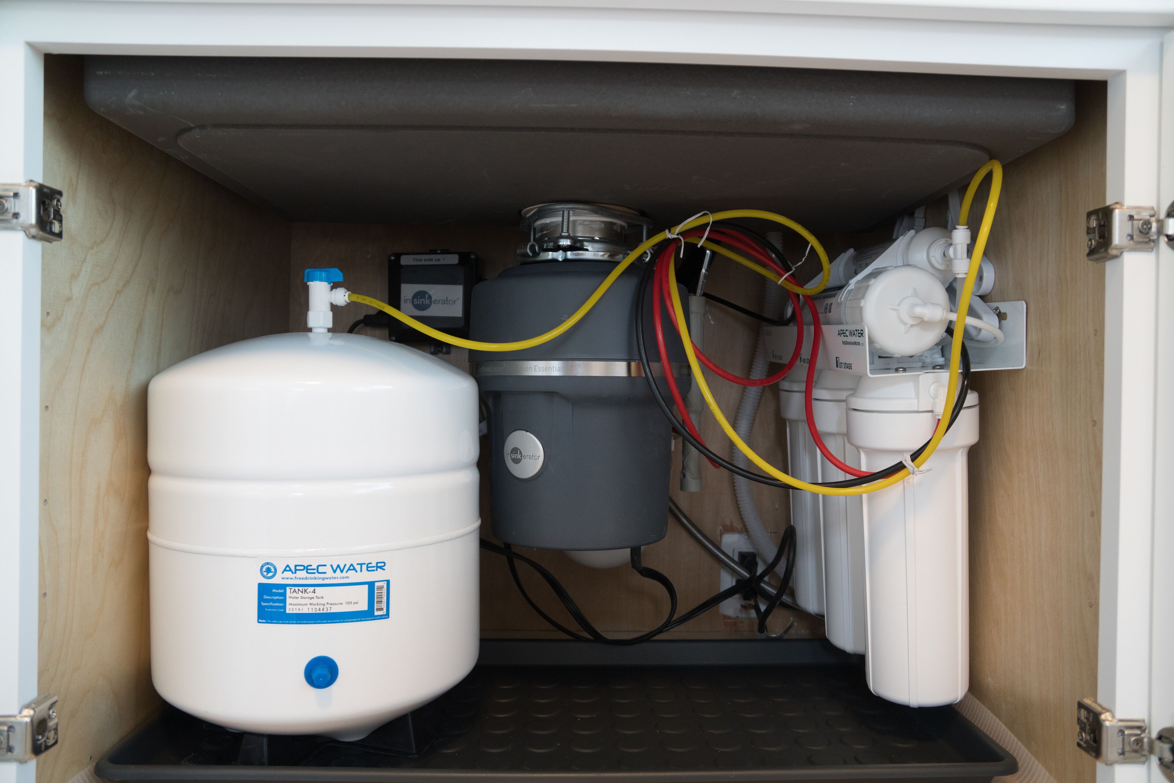 A water filtration system with a large white tank labeled "APEC WATER" and a grey filter unit, connected by multiple hoses.