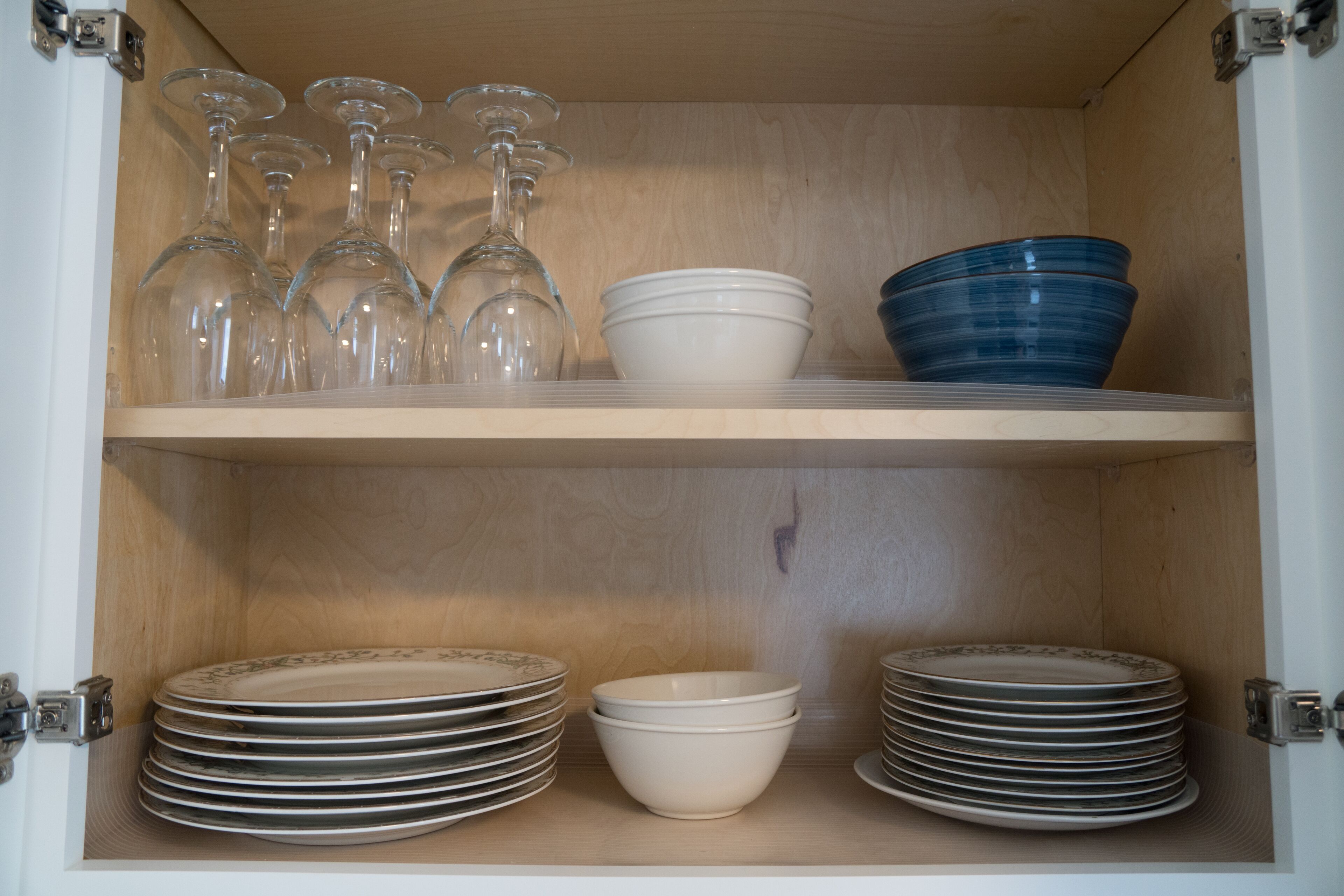 A wooden cabinet with shelves containing glassware, bowls, and stacked plates.