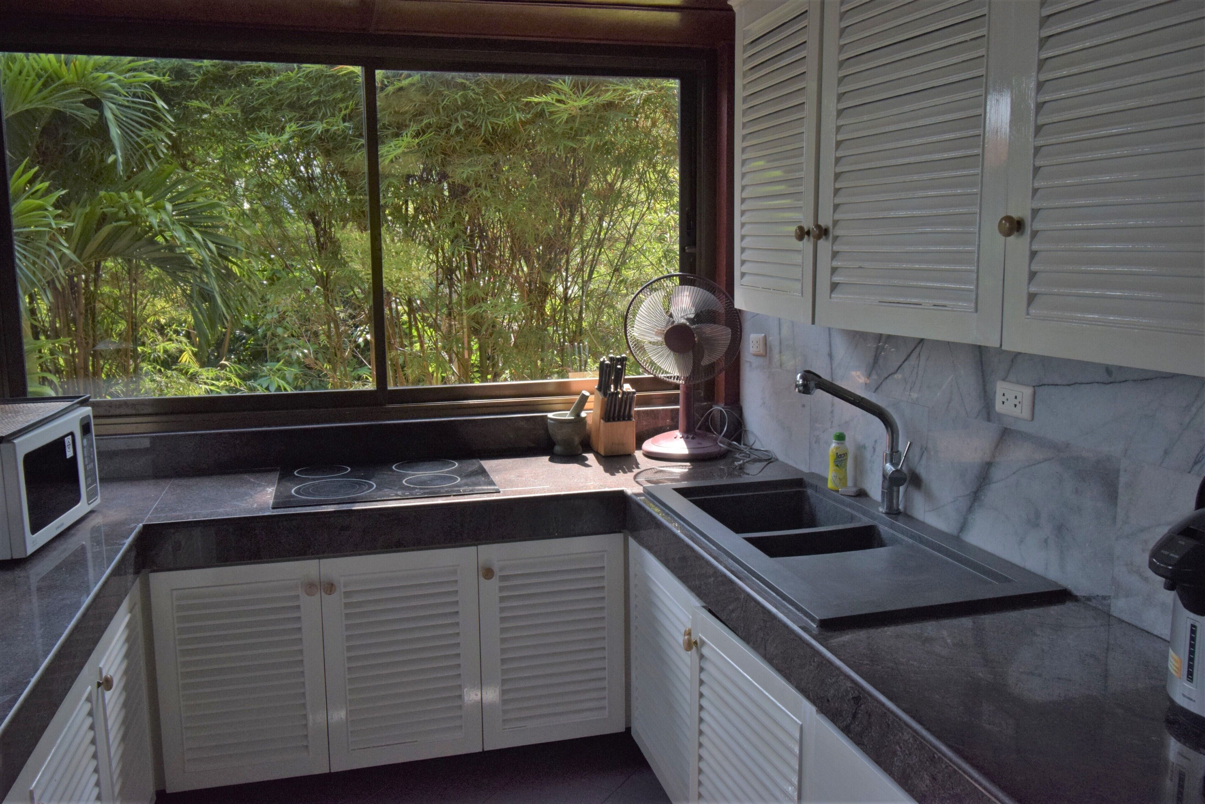 A kitchen with a window, white cabinets, a microwave, a sink, and a fan.