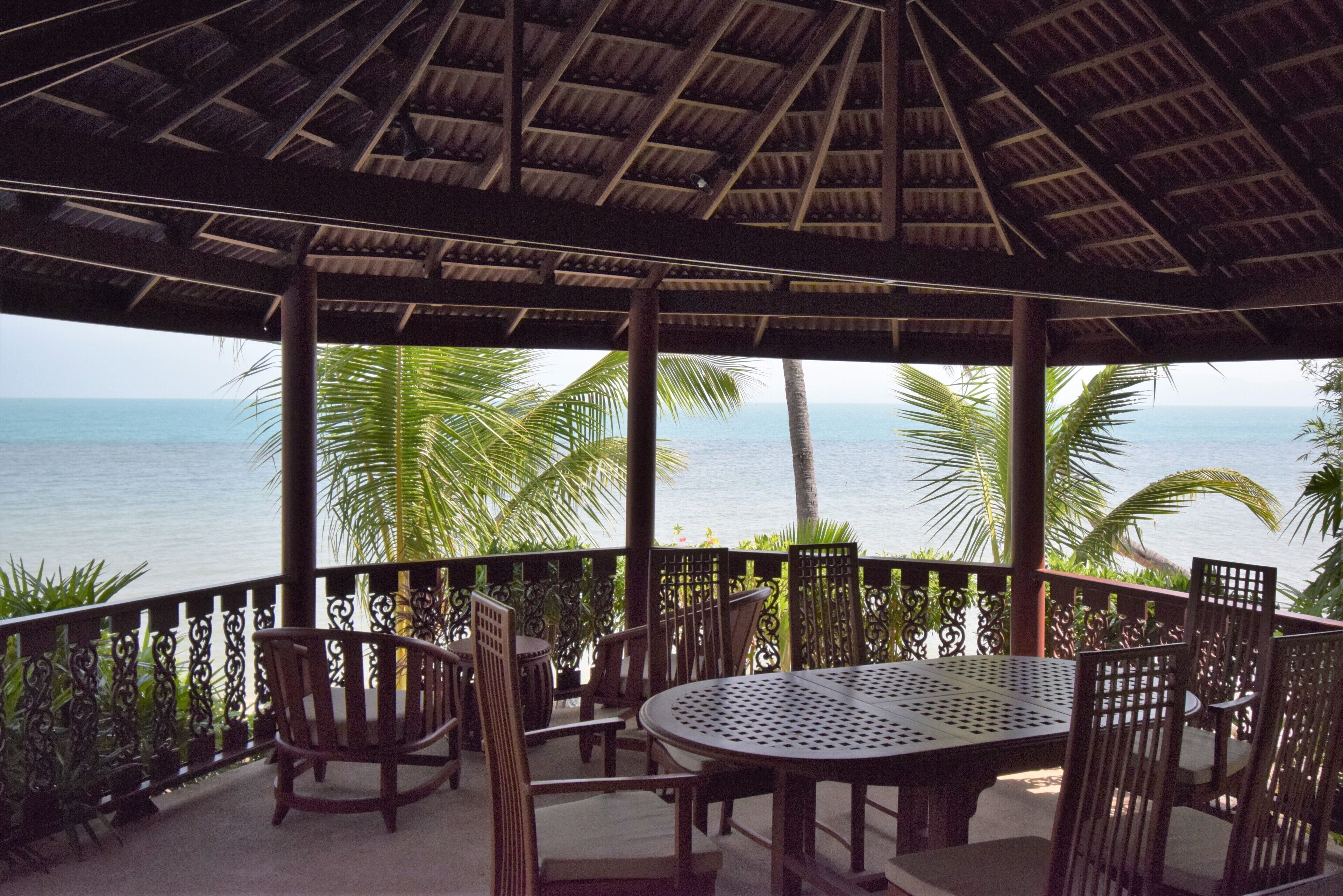 A covered outdoor seating area with a table and chairs, overlooking the ocean.