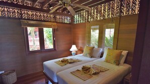 Una habitación con dos camas, ventilador de techo, ventana con vistas a zonas verdes y una lámpara.