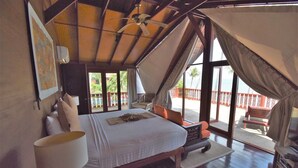 Un dormitorio con cama, ventilador de techo, ventana grande y vista al exterior.