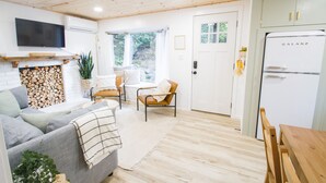 Una sala moderna con un sofá gris, una mesa de comedor de madera y un refrigerador blanco.