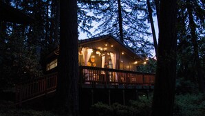 Una cabaña con terraza de madera y ventanas amplias, rodeada de árboles.