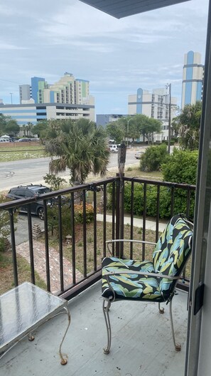 A balcony with a chair, a table, and a view of a parking lot and buildings. - Beachy apartment less than 2 blocks from the beach (Myrtle Beach)