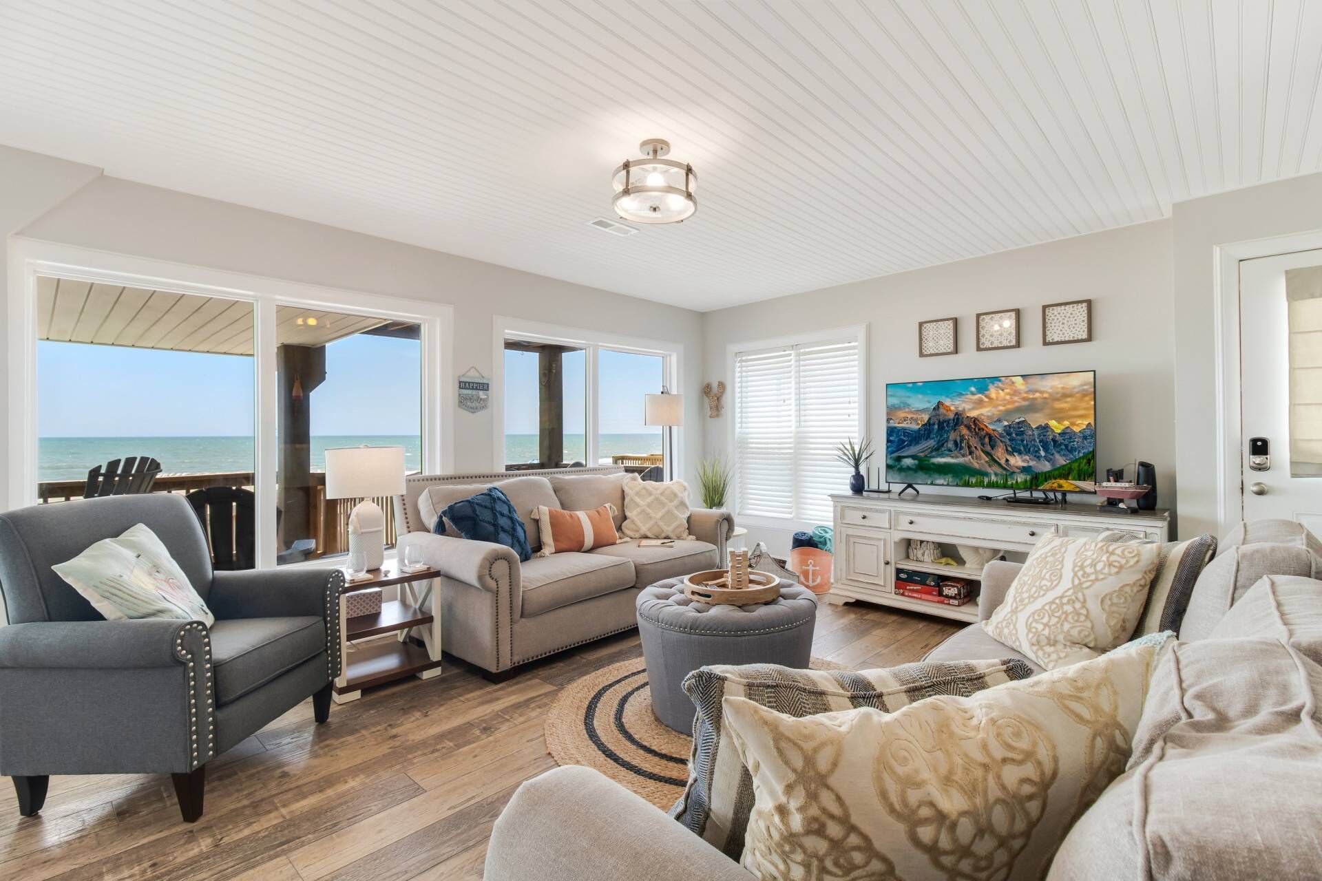 A spacious living room with a view of the ocean, a large flat-screen TV, and a cozy seating area with a fireplace.