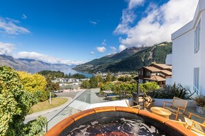 A terrace with wicker furniture, a view of a lake, mountains, and a town in the background. - 6b Edinburgh (Queenstown)