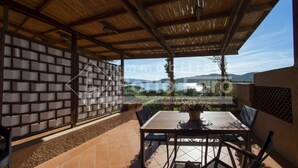 Eine überdachte Terrasse mit Tisch und Stühlen, Blick auf einen See und eine Ziegelwand mit Rasteroptik.