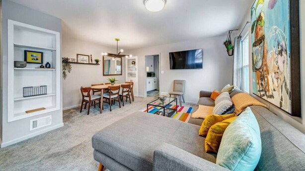 Een moderne woonkamer met een grijze bank, een salontafel en een eethoek met een houten tafel en stoelen.