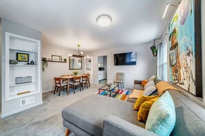 Een moderne woonkamer met een grijze bank, een salontafel en een eethoek met een houten tafel en stoelen.