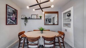 Een eetgedeelte met een ronde tafel, houten stoelen, een kroonluchter, ingelijste kunstwerken en een spiegel.