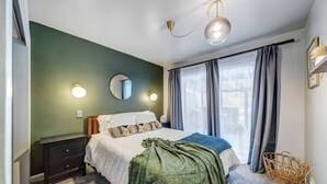 Een slaapkamer met een bed, nachtkastjes, een spiegel en een raam met gordijnen.