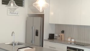 Une cuisine moderne dotée d’un îlot central, de tabourets de bar, d’appareils électroménagers en acier inoxydable et de luminaires suspendus.