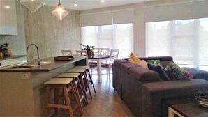 Une cuisine moderne avec un coin bar, une table à manger avec des chaises et un espace salon comprenant un canapé et une table basse.