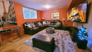 A living room with a sectional sofa, a coffee table, a fireplace, and a large window. - Charming & Cozy Apartment w/ Hot tub patio. (Kenmore)