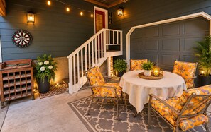 A cozy outdoor seating area with a table and chairs, a dartboard, and a small wooden rack with numbered slots. - Charming & Cozy Apartment w/ firepit & patio. (Kenmore)