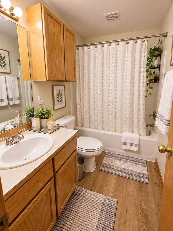 Een badkamer met houten kastjes, een witte wasbak, toilet, bad en douchegordijn.