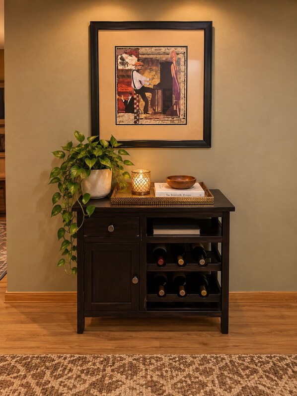 A dark wooden cabinet with wine bottles, a plant, and a framed artwork on the wall. - Charming & Cozy Apartment w/ firepit & patio. (Kenmore)