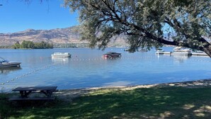A lakeside view with boats, a picnic table, and a tree. - Lakeshore Villas Resort - Three Bedroom Lakefront Condo  (Osoyoos)