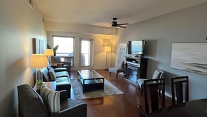 A spacious living room with a sofa, coffee table, and TV. There is a dining table with chairs and a fireplace. - Lakeshore Villas Resort - Three Bedroom Lakefront Condo  (Osoyoos)