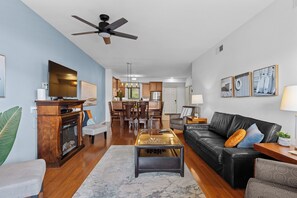 A modern living room with a black leather sofa, a glass coffee table, and a dining area with wooden furniture.