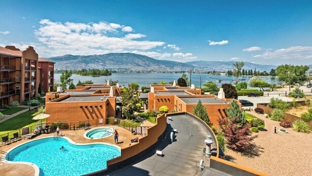 A hotel with a swimming pool, outdoor seating, and a view of mountains and a lake. - Lakeshore Villas Resort - Three Bedroom Lakefront Condo  (Osoyoos)