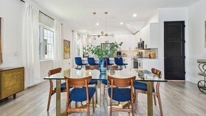 A modern dining area with a glass table, blue chairs, and a central plant.