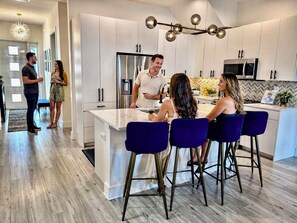 Una cocina moderna con armarios blancos, un refrigerador de acero inoxidable y una zona de bar con taburetes azules.