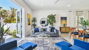 A modern living room with a grey sofa, blue chairs, a glass coffee table, and a dining area with wooden chairs and a glass table.