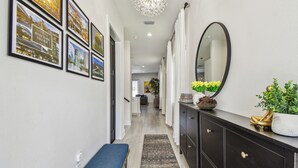 A hallway with framed pictures on the wall, a bench, a mirror, and a potted plant.
