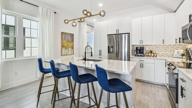 A modern kitchen with white cabinets, a stainless steel refrigerator, and a central island with blue bar stools.