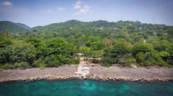 A coastal landscape with a rocky shoreline, dense greenery, and a clear view of the sea.