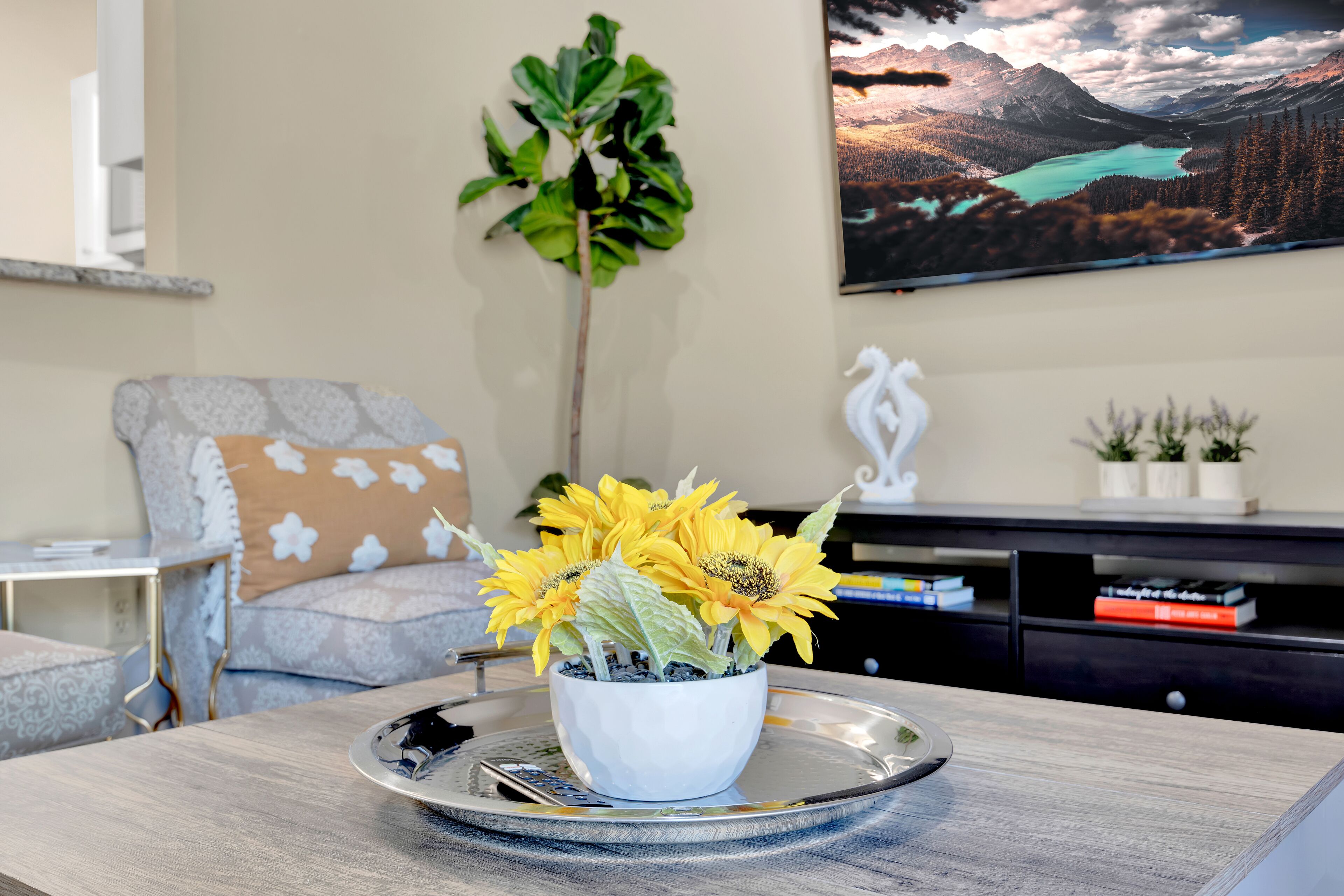 A living room with a coffee table, a sofa, a potted plant, and a painting on the wall.