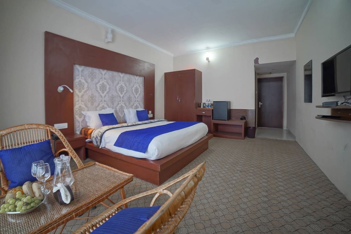 Habitación de hotel con cama, televisión, escritorio, silla y mesa de comedor con frutas.