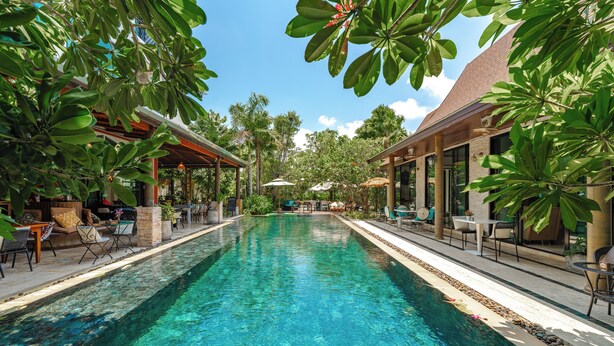 A clear blue pool with lounge chairs and umbrellas on both sides, surrounded by lush greenery and a covered seating area. - Coco Paradiso Phuket Hotel (Chalong)