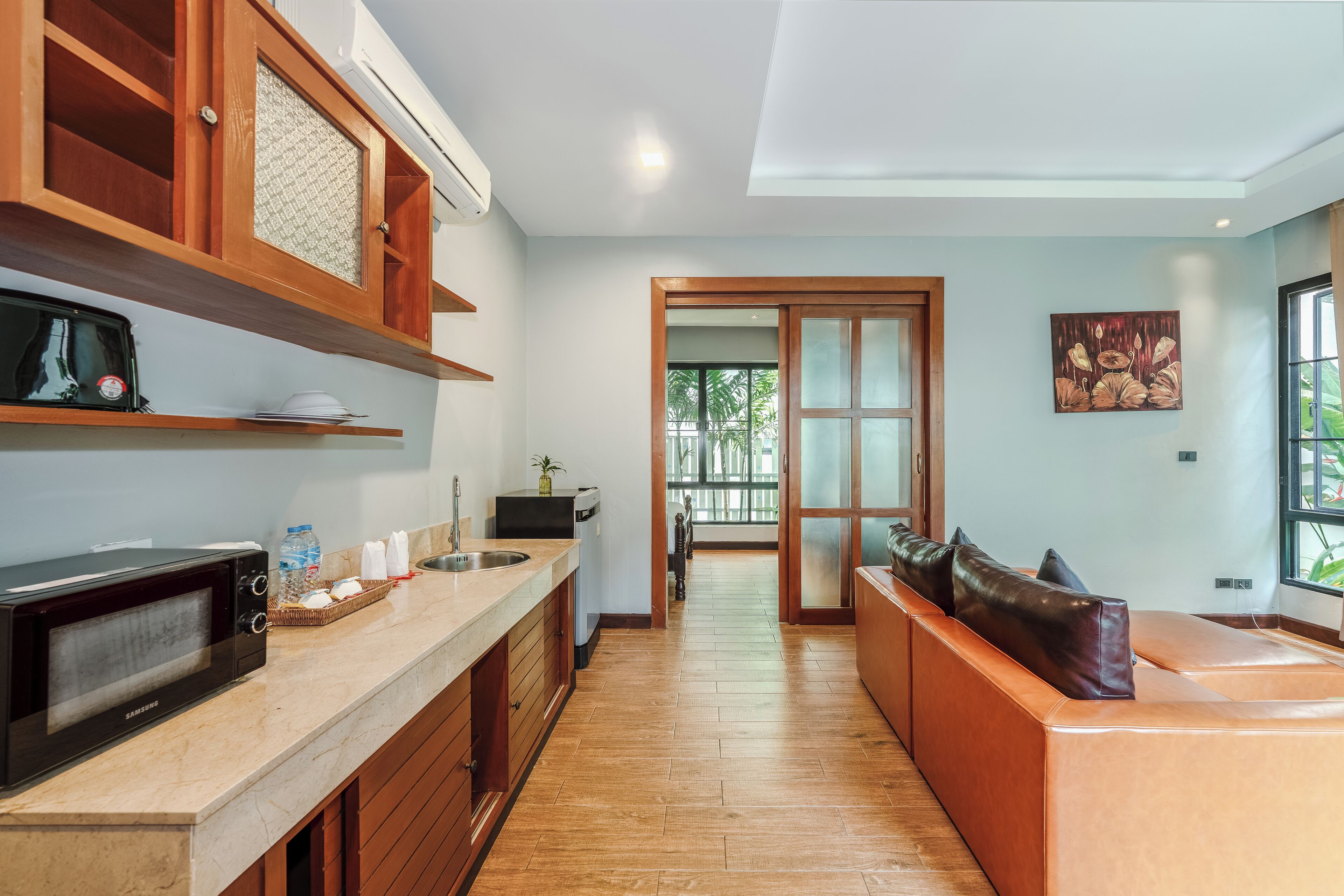 A modern kitchen with a microwave, toaster, and a water dispenser. There is a wooden cabinet with a glass door, a sink, and a countertop with a basket of bread.