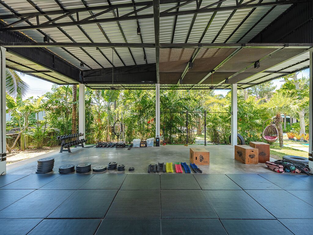 A covered outdoor gym area with exercise equipment, including dumbbells, weight plates, and resistance bands.