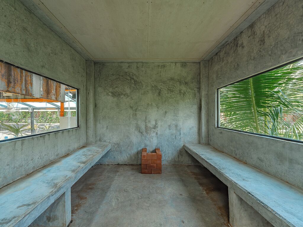 A room with concrete walls, a bench, and a window with a view of palm trees.