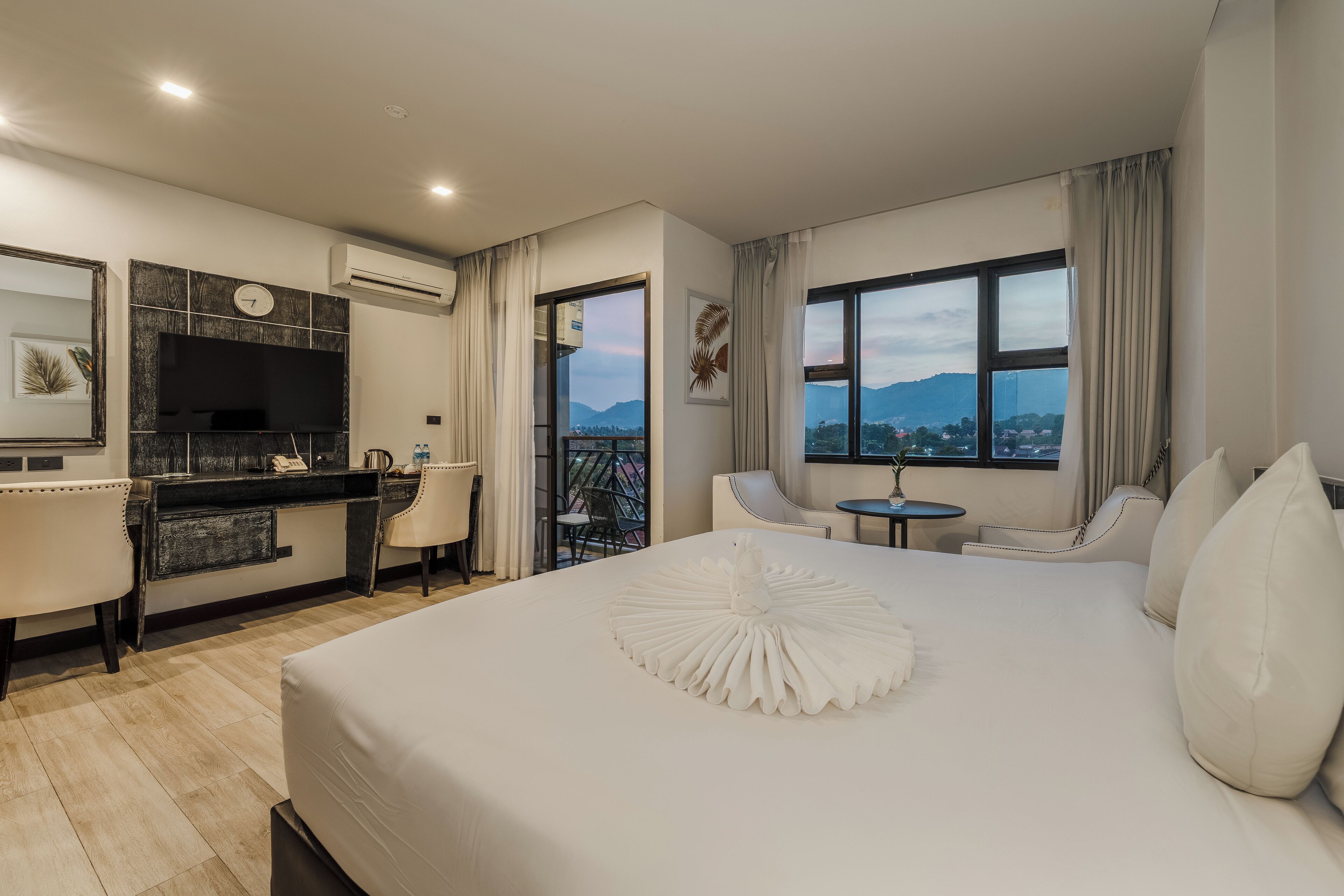 A modern hotel room with a large bed, a desk, and a balcony with a view of the mountains.
