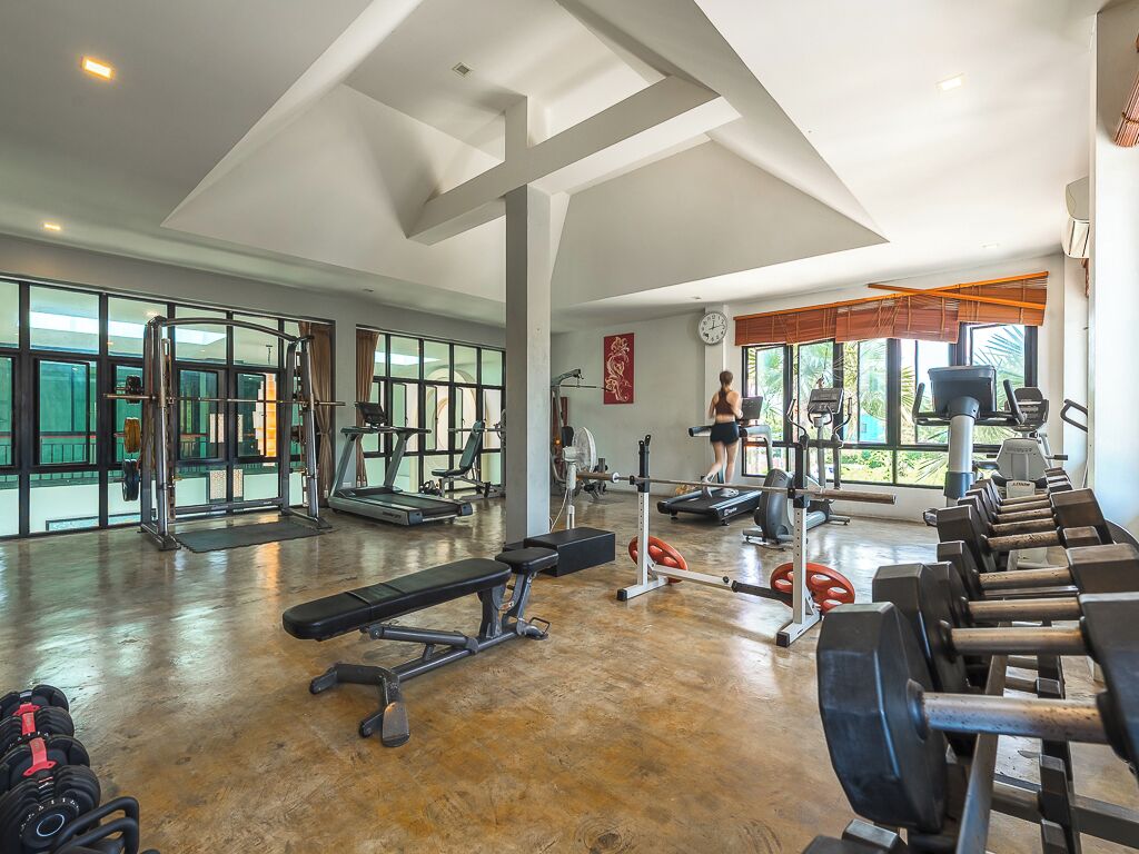 A spacious gym with various exercise equipment, large windows, and a high ceiling.