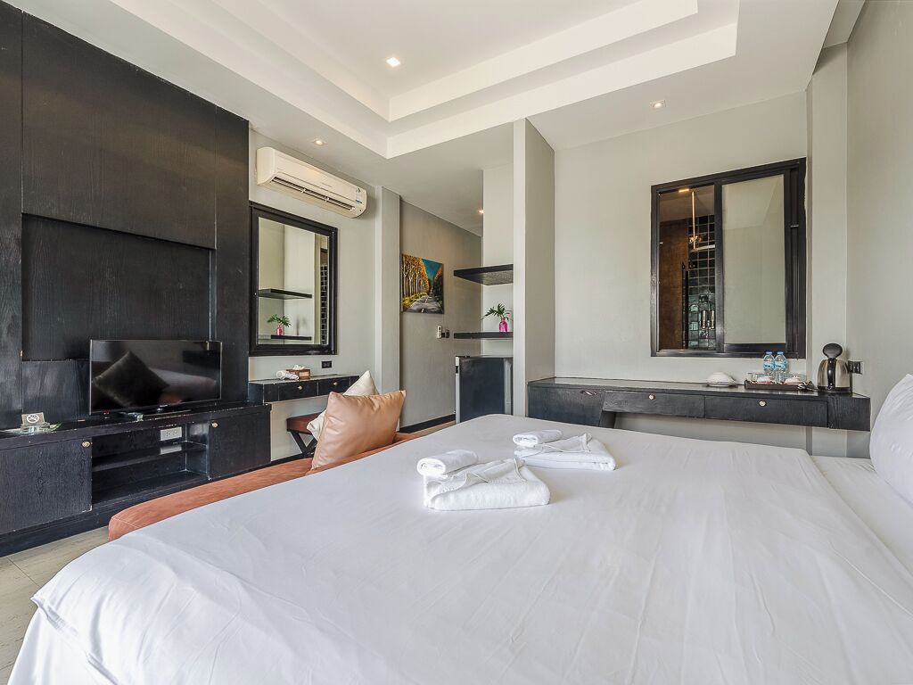 Una habitación de hotel moderna con una cama grande, televisor de pantalla plana, escritorio y baño con espejo.