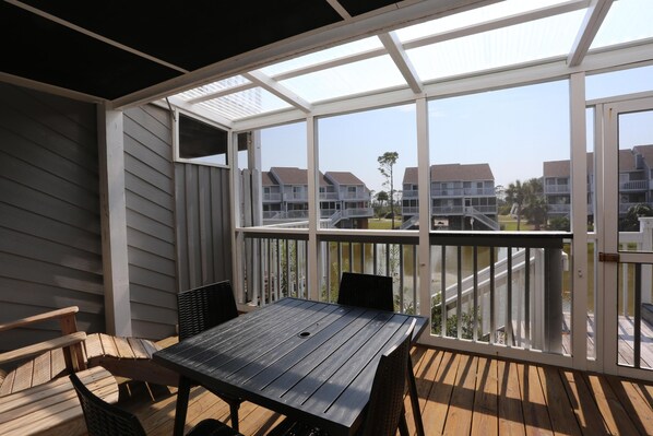 A covered outdoor deck with a table and chairs, overlooking a residential area with multiple buildings.