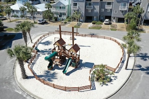 Children can play on the slide and climbing structures in this enclosed playground surrounded by palm trees.