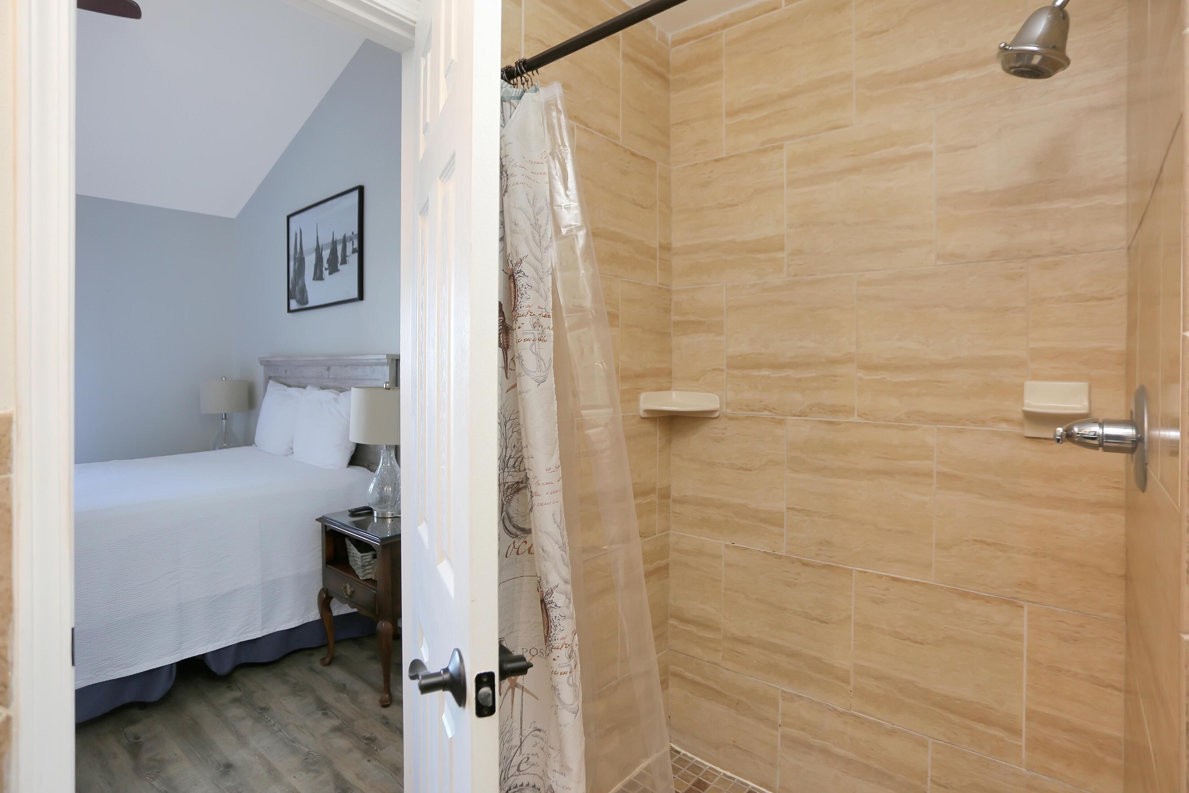 Un dormitorio con cama, mesita de noche y baño con ducha.