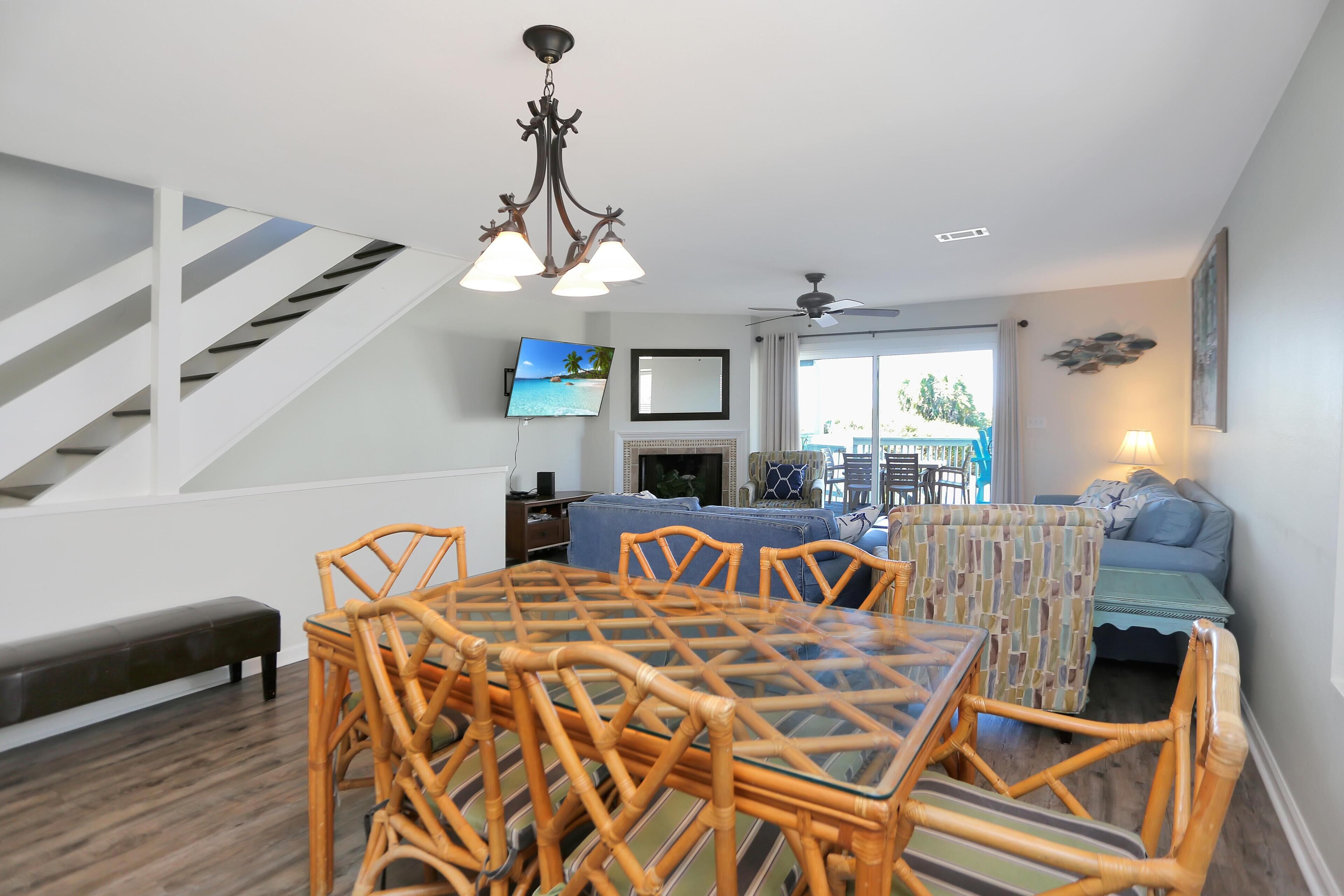 A modern living room with a glass-top dining table, wicker chairs, a sofa, and a staircase.