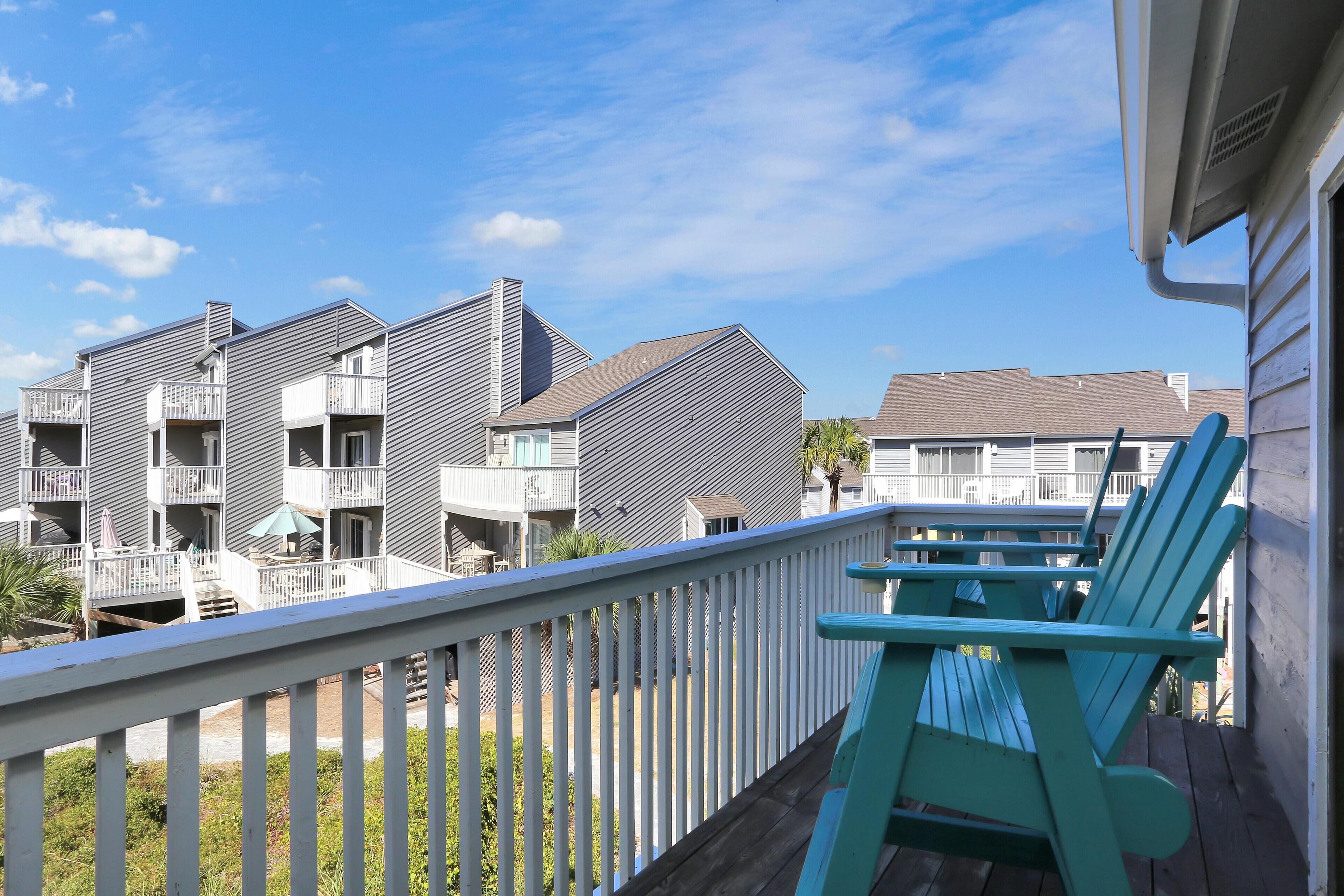 A balcony with a white railing and turquoise Adirondack chairs.