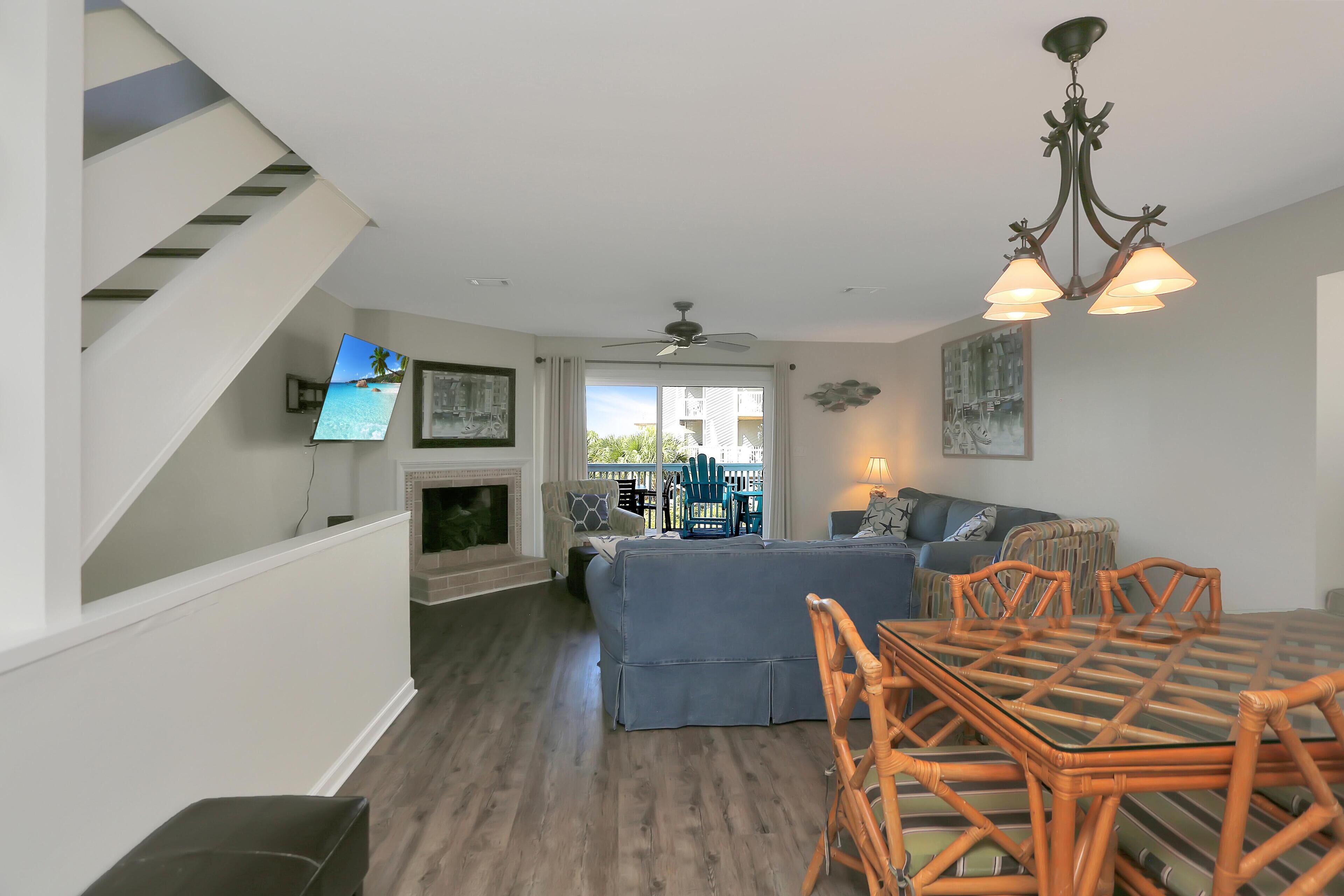 A spacious living room with a staircase, a fireplace, a blue sofa, a dining table with chairs, and a ceiling fan.