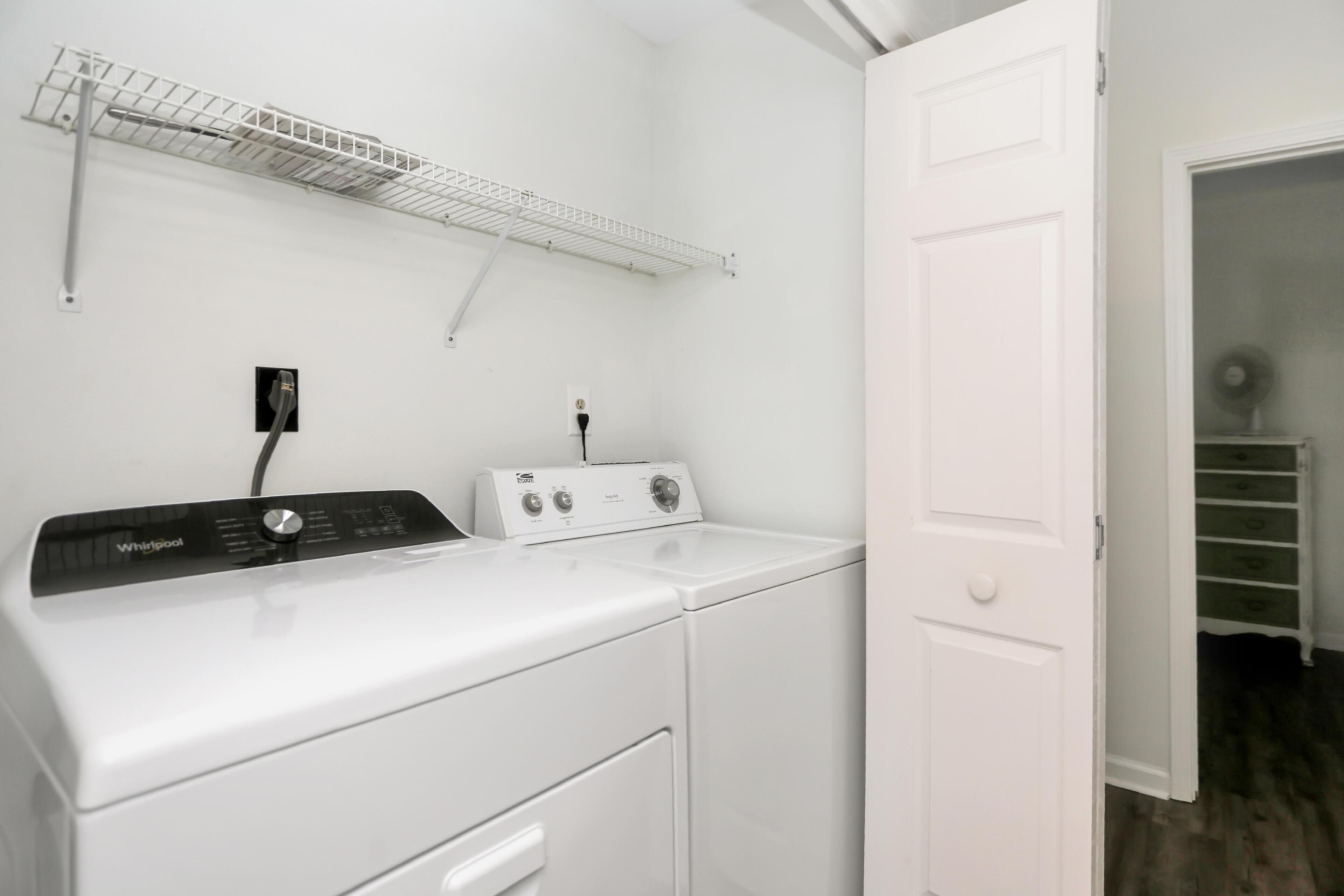 Zona de lavandería con lavadora y secadora Whirlpool, un tendedero metálico y una puerta blanca que da a un armario.
