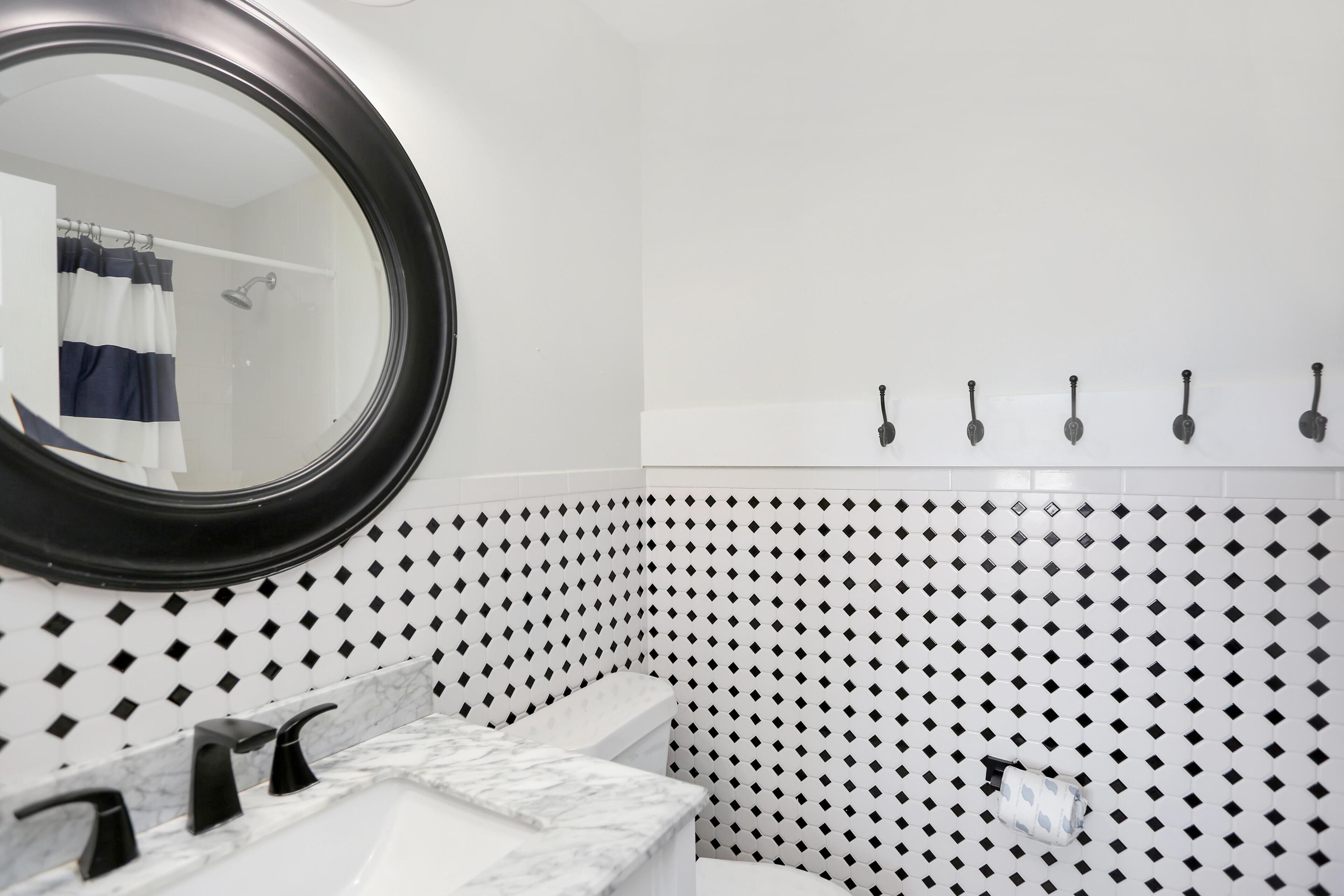 A bathroom with a white sink, black faucets, a round mirror, and a shower with a curtain.