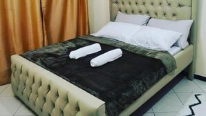 Ein Schlafzimmer mit einem geblümten Kopfteil, einem Bett mit weißen Leinen und einer schwarzen Tagesdecke.